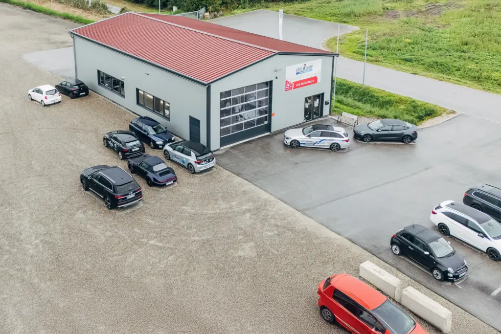 Moderne Werkstatthalle von Rucker 2 mit mehreren geparkten Autos auf dem Firmengelände